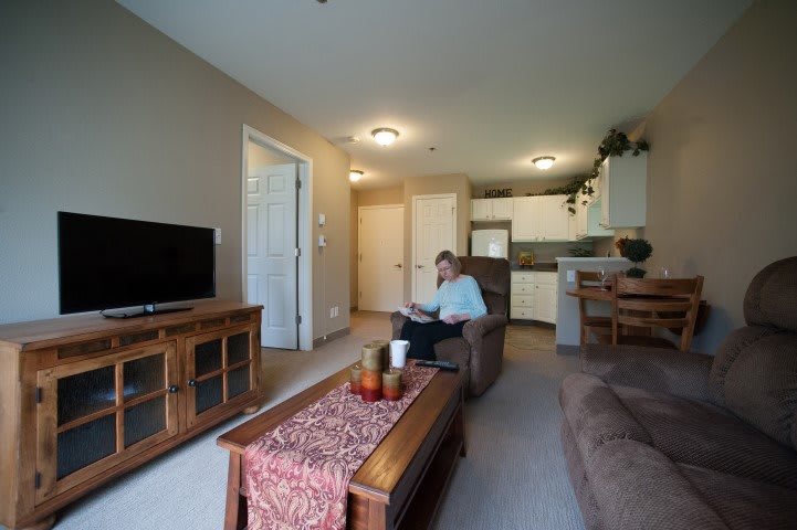 A cozy living room with a television, sofa, and coffee table, leading into a small kitchen area.