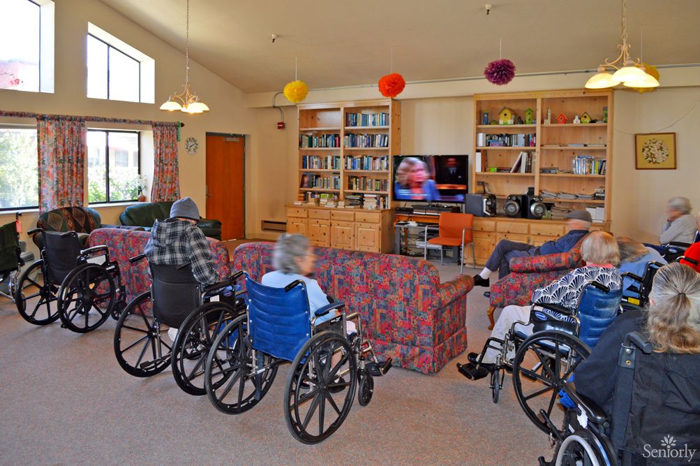 Elderly residents in a nursing home are watching television together in a communal living room.
