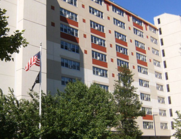 A multi-story apartment building with a flagpole and surrounding trees.