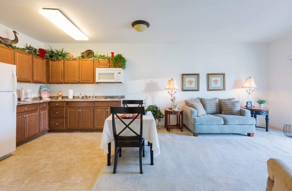 A cozy open-plan living area with a small dining table, kitchen, and comfortable sofa.