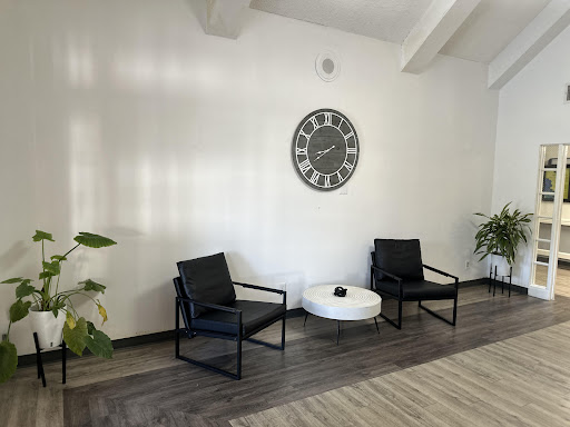 A modern waiting area featuring black chairs, a round coffee table, and decorative plants.