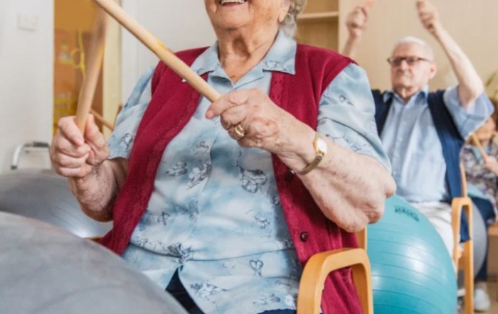 Elderly individuals participating in a group exercise session using sticks.