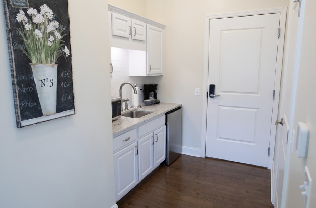 A compact kitchen area featuring white cabinets, a coffee maker, and a sink.