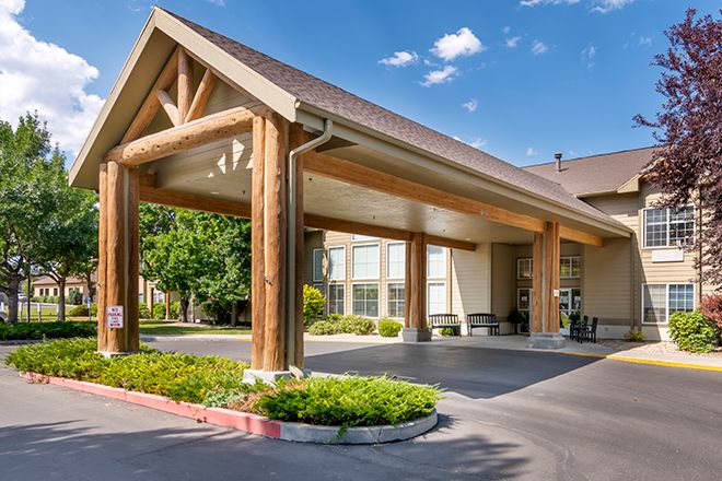 A hotel entrance with a wooden frame and a covered driveway surrounded by greenery.