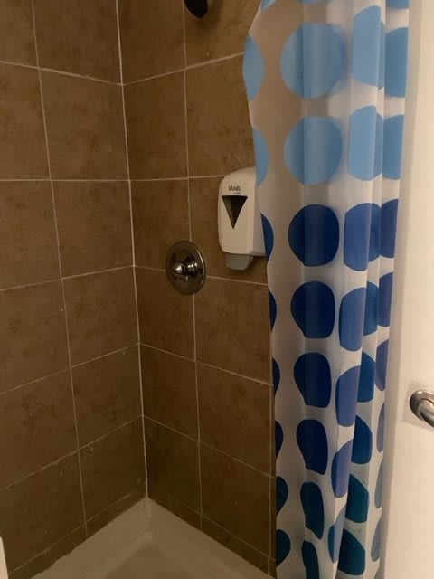 A bathroom shower with a blue polka dot curtain and tile walls.