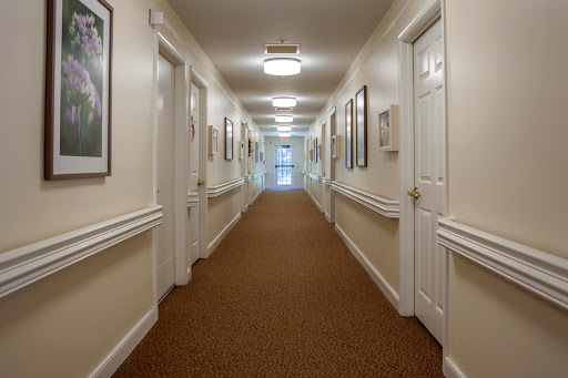A long, well-lit hallway with beige walls and carpeting, lined with doors and framed pictures.