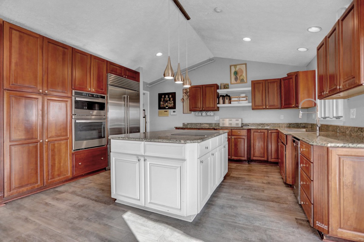 A modern and spacious kitchen featuring a white island, wood cabinets, and stainless steel appliances.