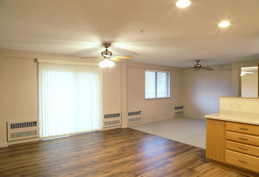 A spacious living room featuring wood flooring, large windows, and ceiling fans.
