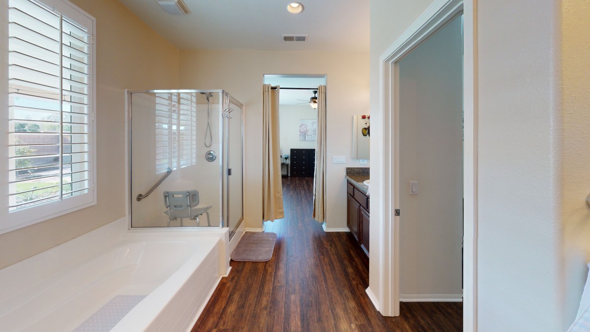 A modern bathroom with a bathtub and separate shower area, featuring hardwood floors and bright lighting.