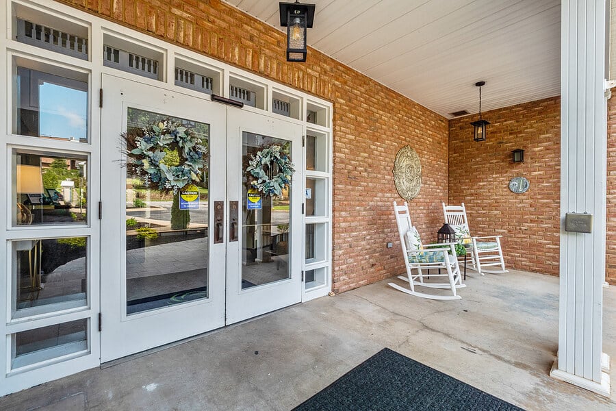 A welcoming porch with double glass doors adorned with wreaths and two white rocking chairs.
