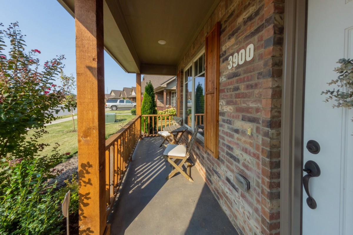 A cozy front porch with wooden chairs and brick walls, overlooking a peaceful neighborhood.