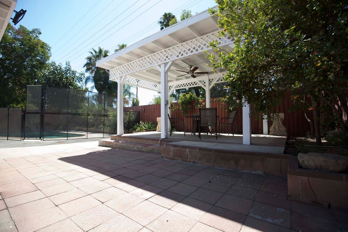 A sunny backyard with a white pergola providing shade over a tiled patio area.
