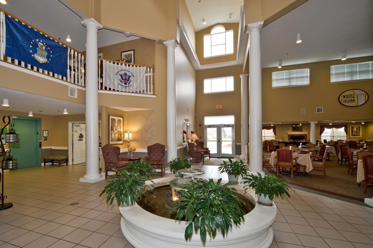 A spacious and elegant hotel lobby with tall columns, a central plant display, and comfortable seating areas.