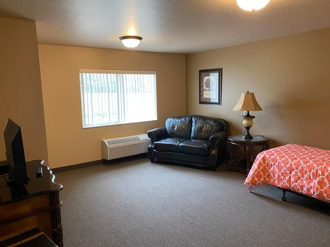 A cozy apartment room with a bed, sofa, and a window providing natural light.