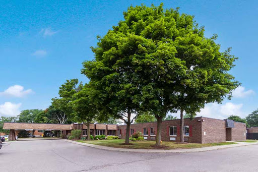 A peaceful view of a brick building surrounded by lush green trees under a clear blue sky.