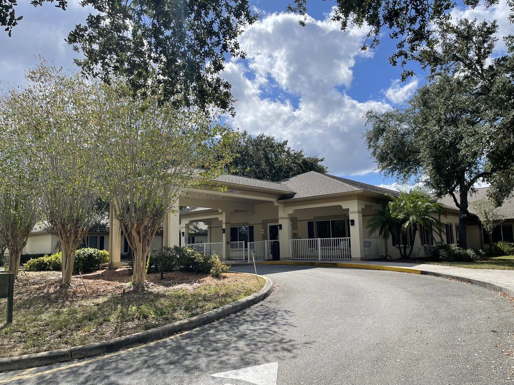 A building with a driveway surrounded by trees under a partly cloudy sky.