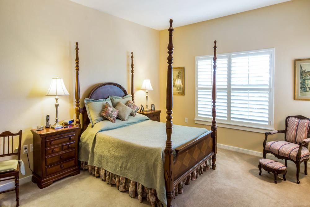 A cozy bedroom featuring a four-poster bed, wooden furniture, and soft lighting from table lamps.
