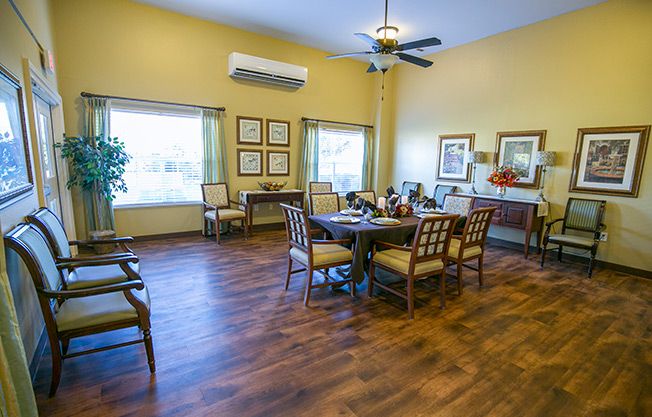 A cozy dining room with wooden floors, a dining table, and chairs, featuring windows and a ceiling fan.