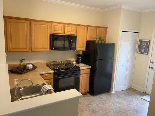 A modern kitchen with wooden cabinets, black appliances, and a tiled floor.