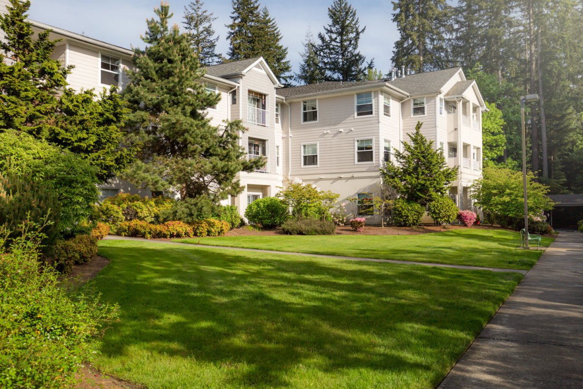 A residential apartment building surrounded by a lush green lawn and trees.