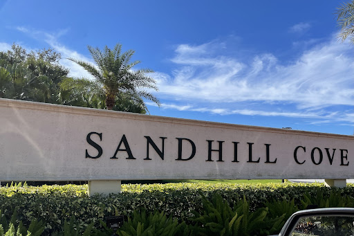 A view of the Sandhill sign against a clear blue sky, surrounded by lush greenery and palm trees.