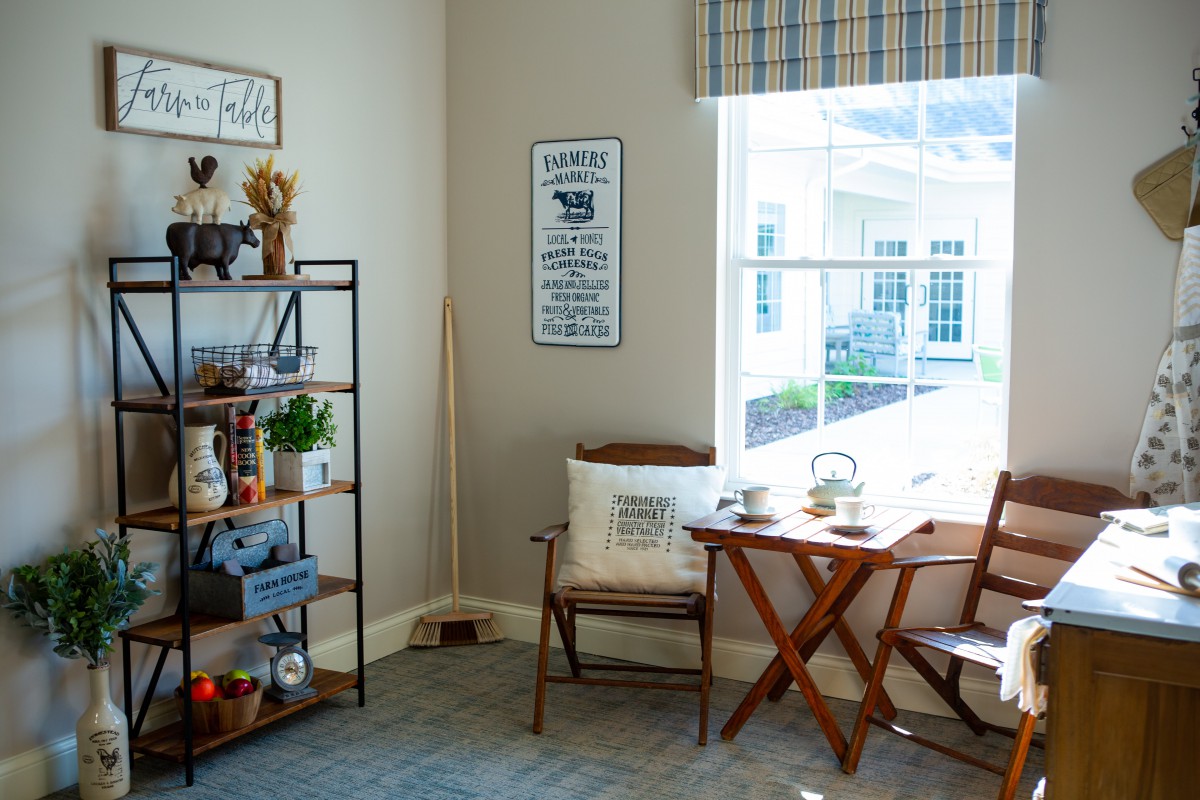 A cozy living room corner with a wooden chair, a small table, and a decorative shelf beside a large window.