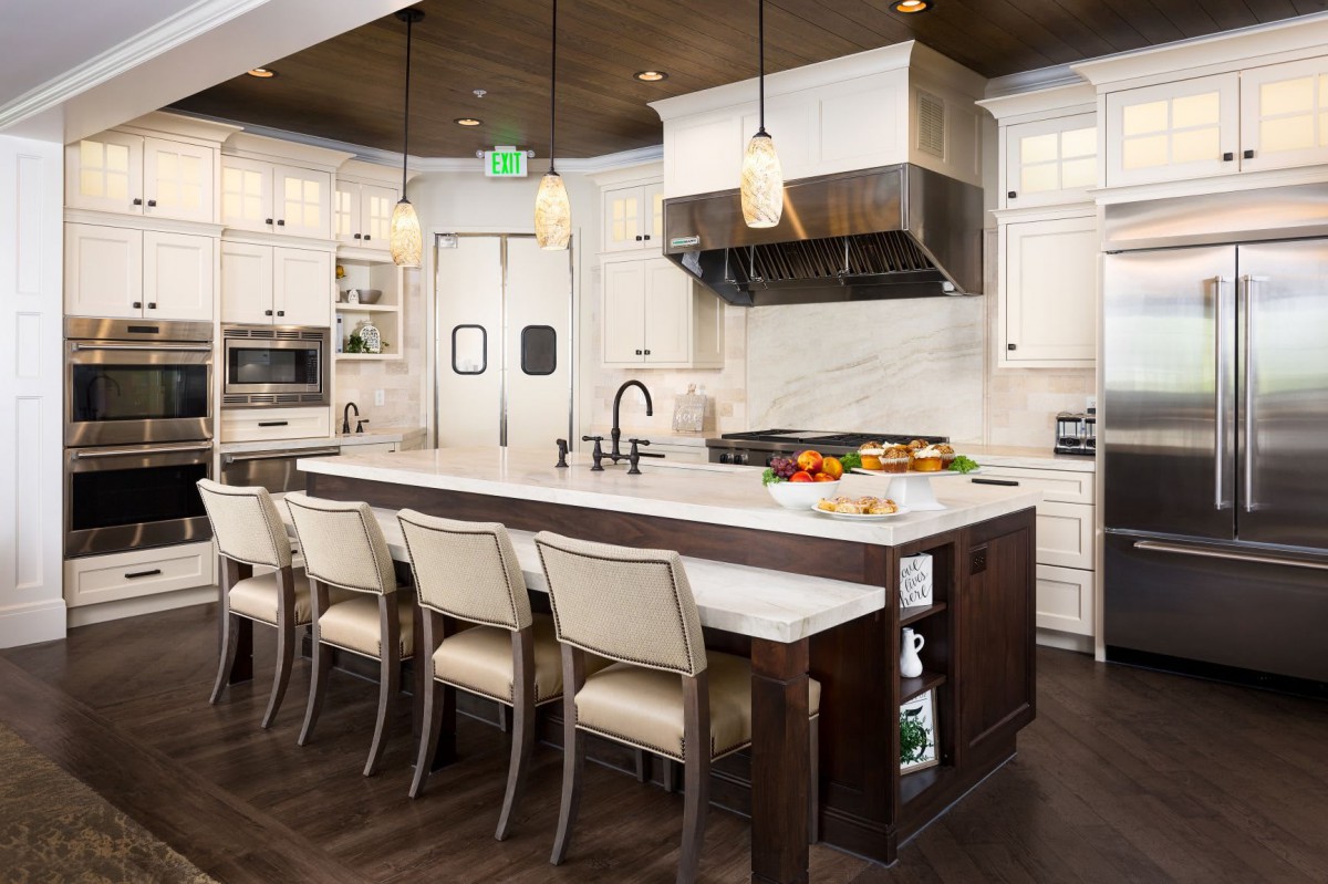 A modern kitchen featuring a large island with bar stools, white cabinets, and stainless steel appliances.