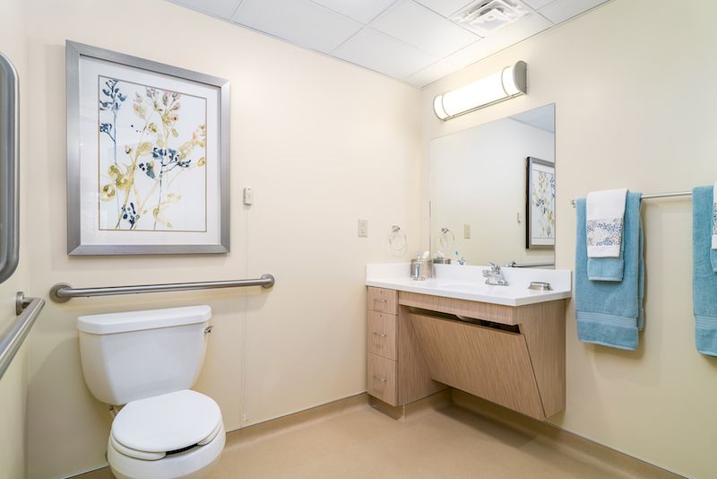 A clean and modern bathroom with a toilet, sink, mirror, and wall art.