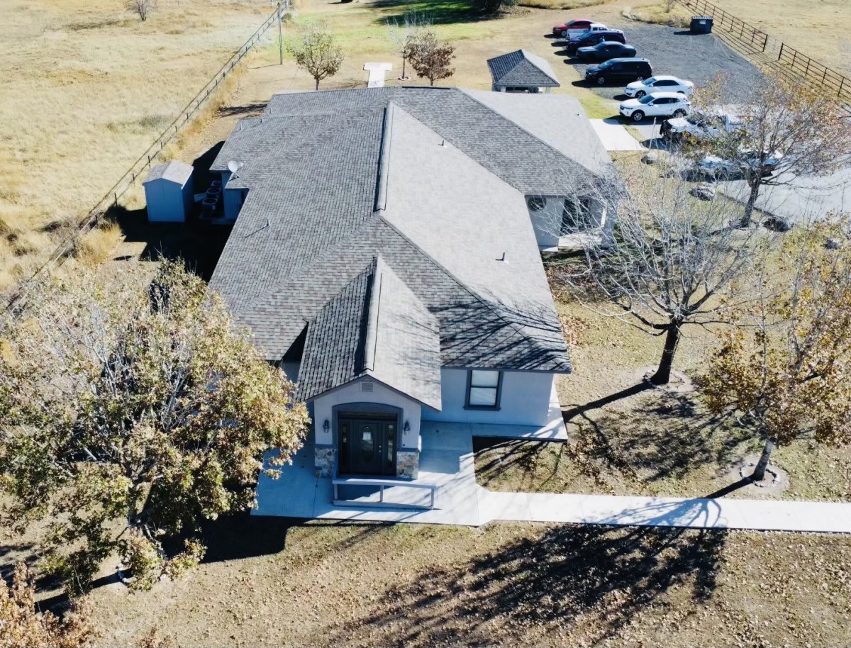 An aerial view of a residential building with a driveway and surrounding trees.
