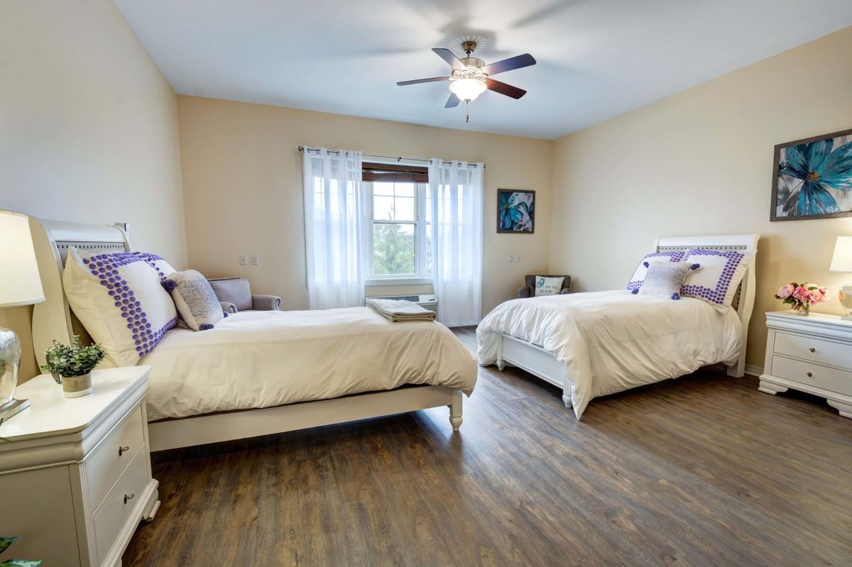 A spacious bedroom with two double beds, featuring a ceiling fan and large window.