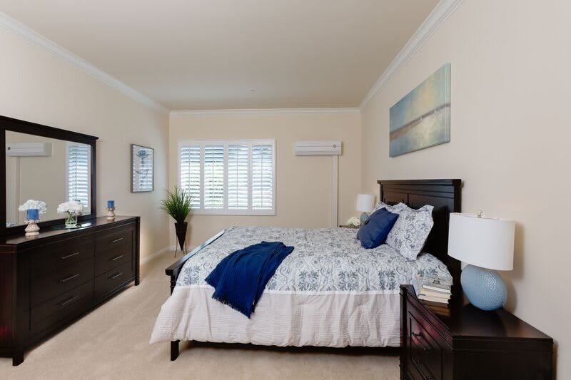 A modern bedroom with a neatly made bed, artwork on the wall, and a large window with shutters.
