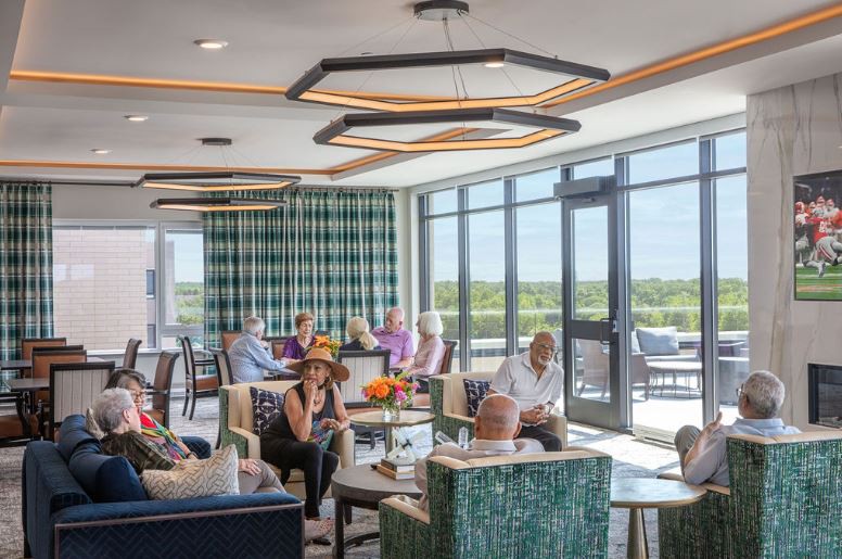 A modern lounge area with people seated, enjoying the bright natural light from large windows.