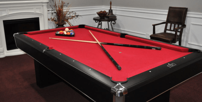 A red-felt pool table with cue sticks crossed on top and a rack of billiard balls.