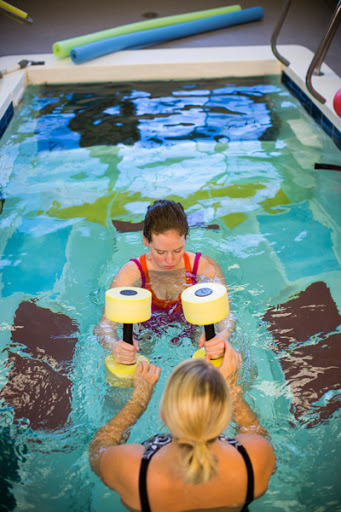 A woman engages in aquatic therapy using water weights with the assistance of another person.
