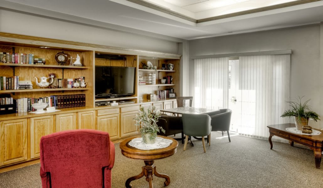 A cozy living room featuring a wooden bookshelf, table with chairs, and a television.
