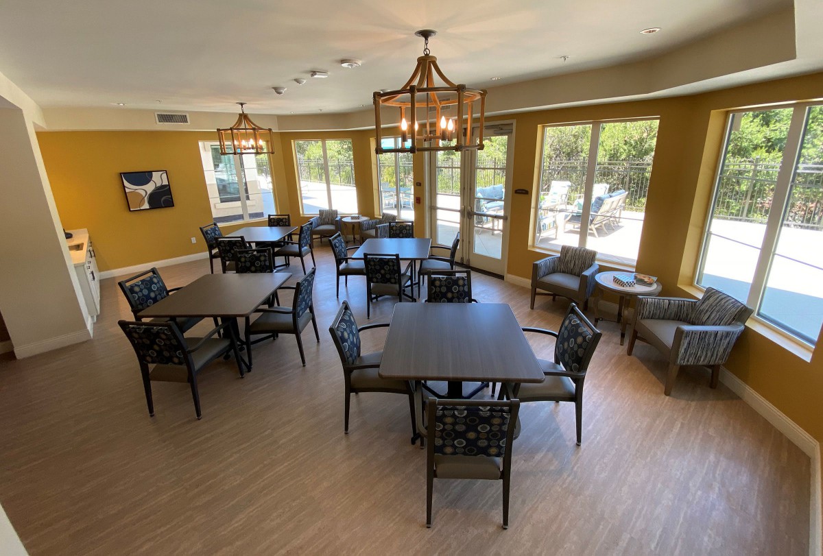 A spacious dining room with multiple tables and chairs, large windows, and elegant lighting fixtures.