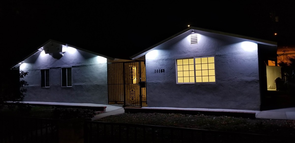 A small house illuminated at night with visible windows and a gated entrance.