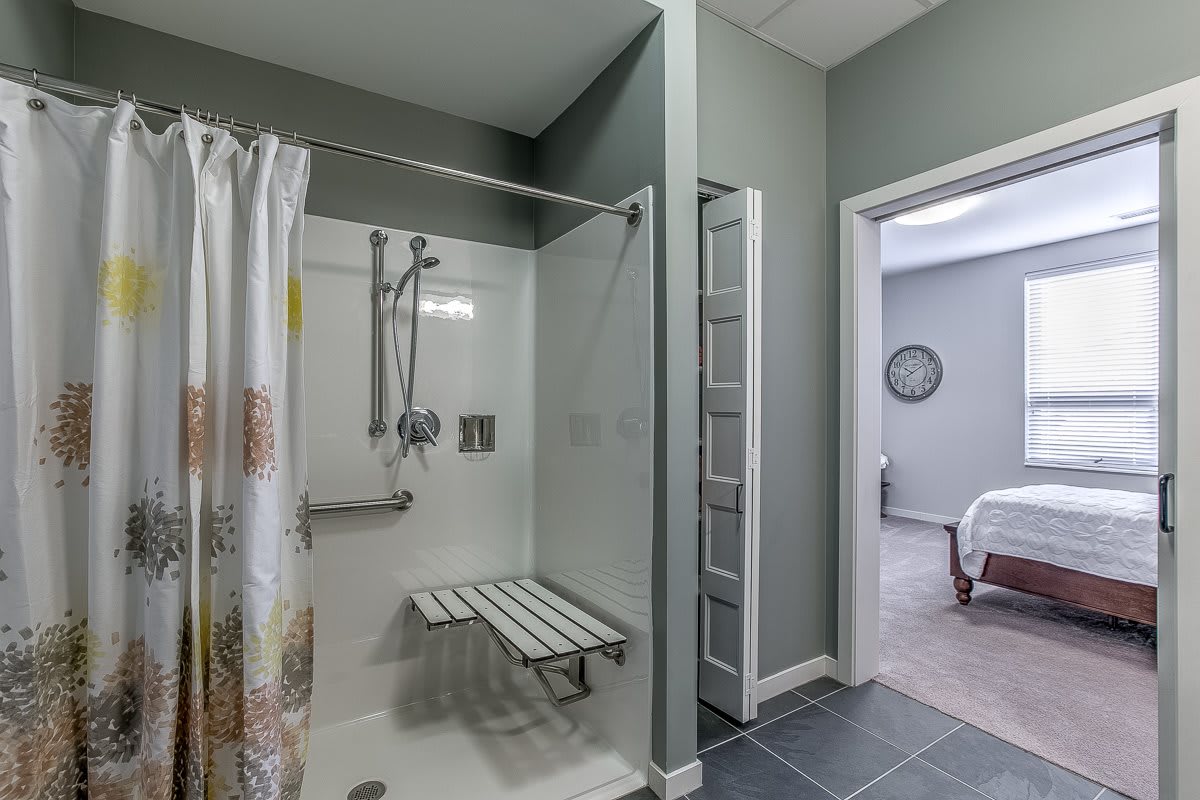 An accessible bathroom featuring a walk-in shower with a folding seat and grab bars.