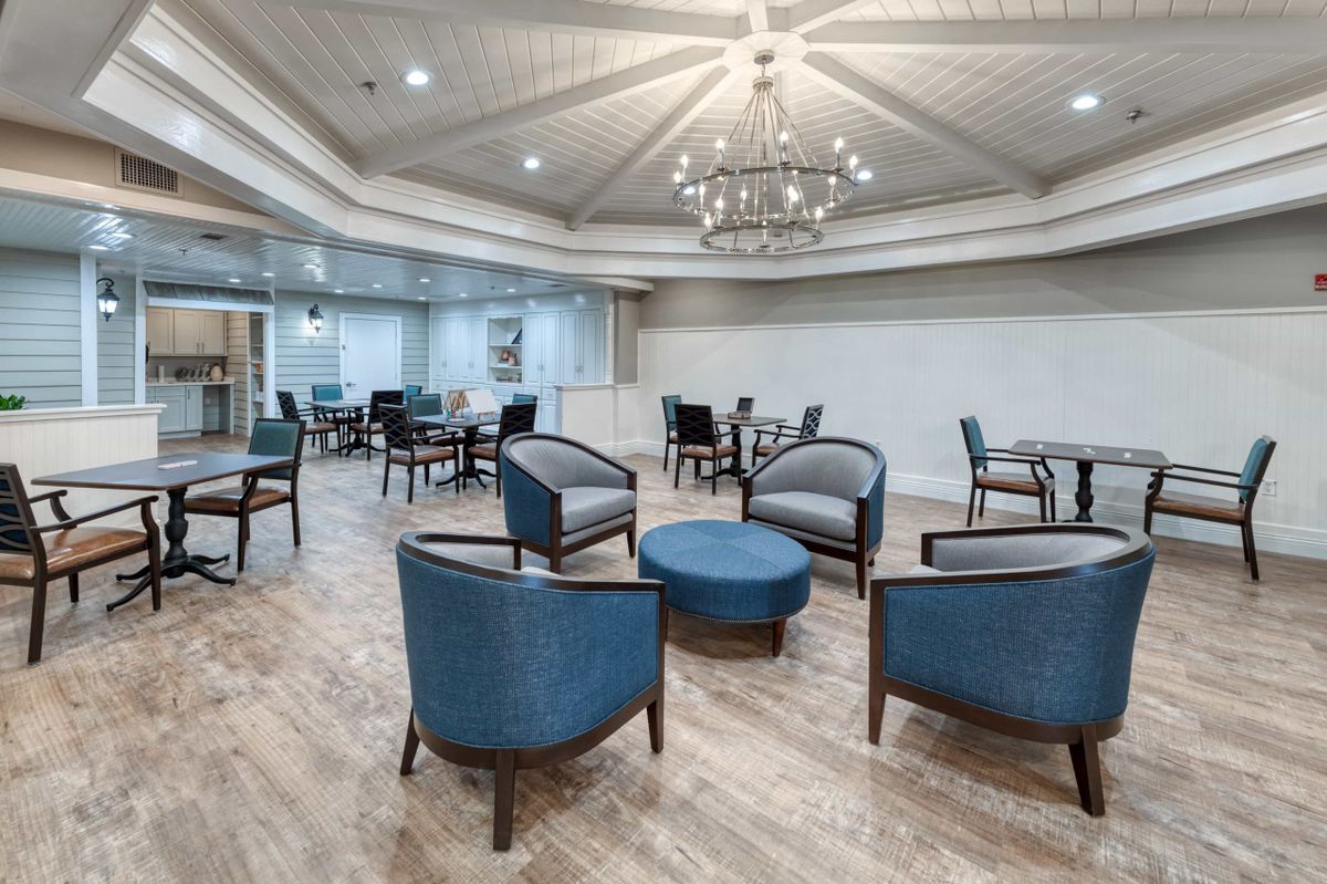 A modern lounge area featuring comfortable chairs, elegant tables, and a chandelier under a high ceiling.