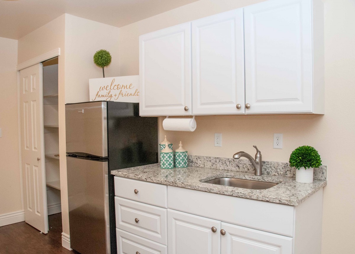 A modern kitchen with white cabinets, granite countertops, and stainless steel refrigerator.