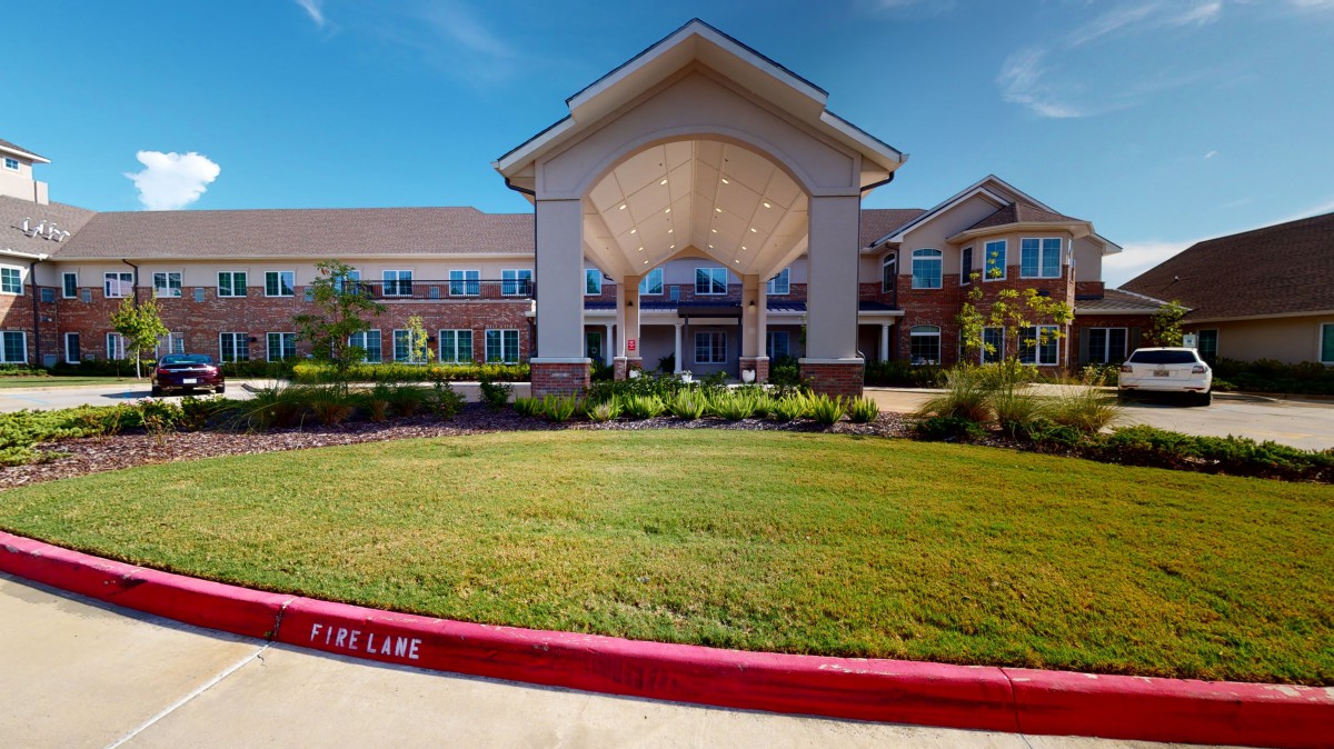 A well-maintained building with a grand entrance and landscaped surroundings under a clear blue sky.