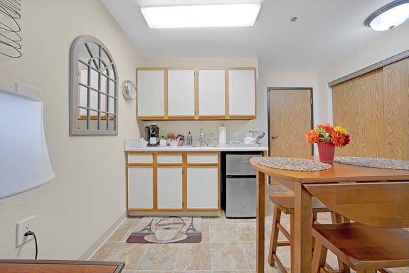 A modern kitchen interior with wooden cabinets, a small refrigerator, and a dining area.