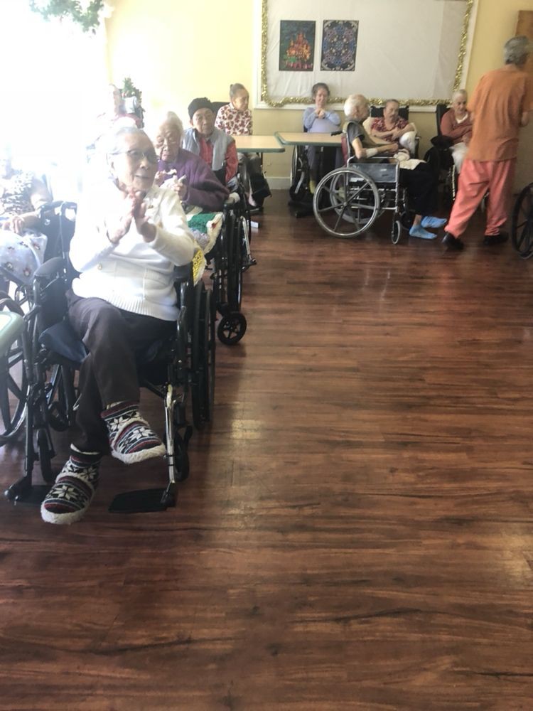A group of elderly individuals gathered in a nursing home, many in wheelchairs, engaged in a community activity.