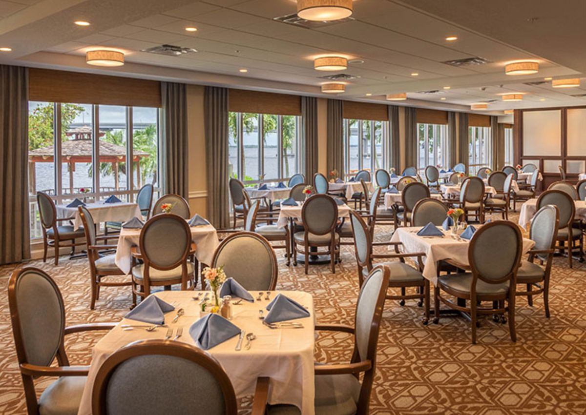 An elegant dining room setup with neatly arranged tables and chairs, featuring large windows and decorative napkins.