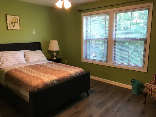 A cozy bedroom featuring a comfortable bed, green walls, and ample natural light from the windows.
