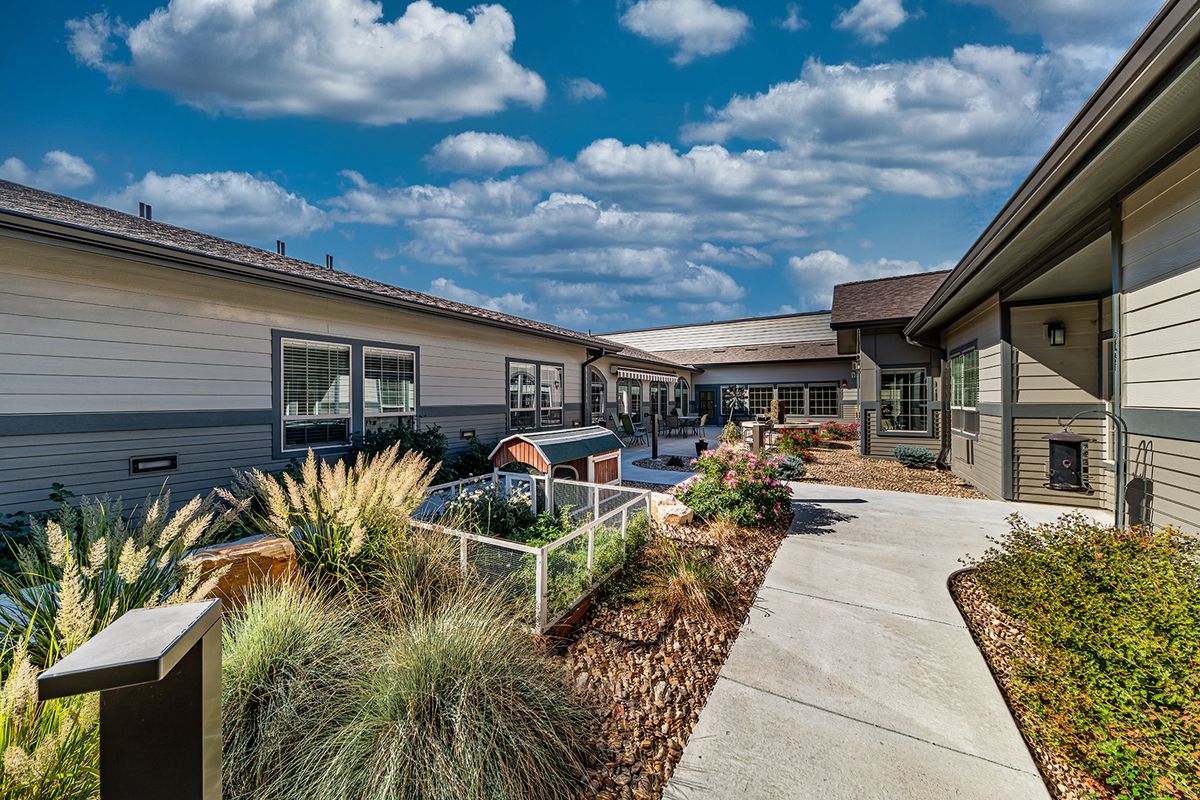 A well-maintained outdoor garden area with a pathway leading between buildings under a partly cloudy sky.