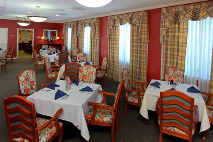 A cozy dining room with neatly arranged tables and chairs, featuring elegant curtains and warm decor.