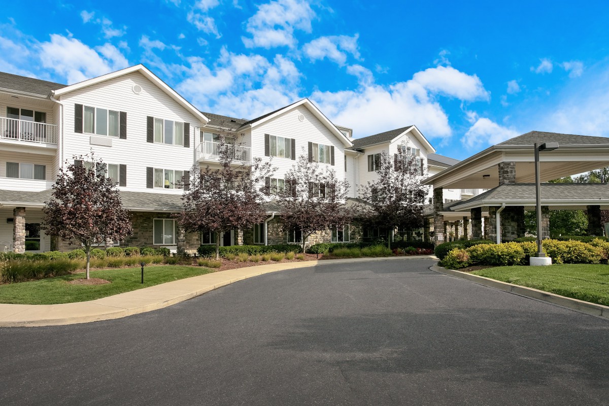 A large residential building with a driveway and landscaped surroundings under a partly cloudy sky.