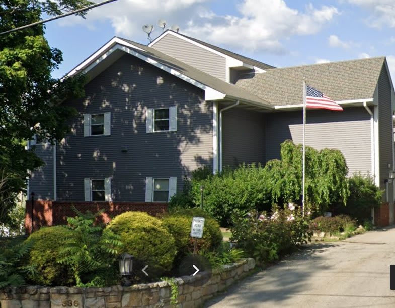 A residential house with a garden and an American flag under a cloudy sky.