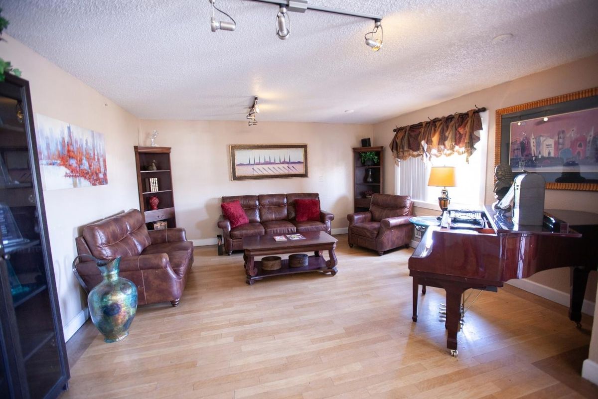 A cozy living room featuring leather sofas, a coffee table, and a piano beside a window with drapes.